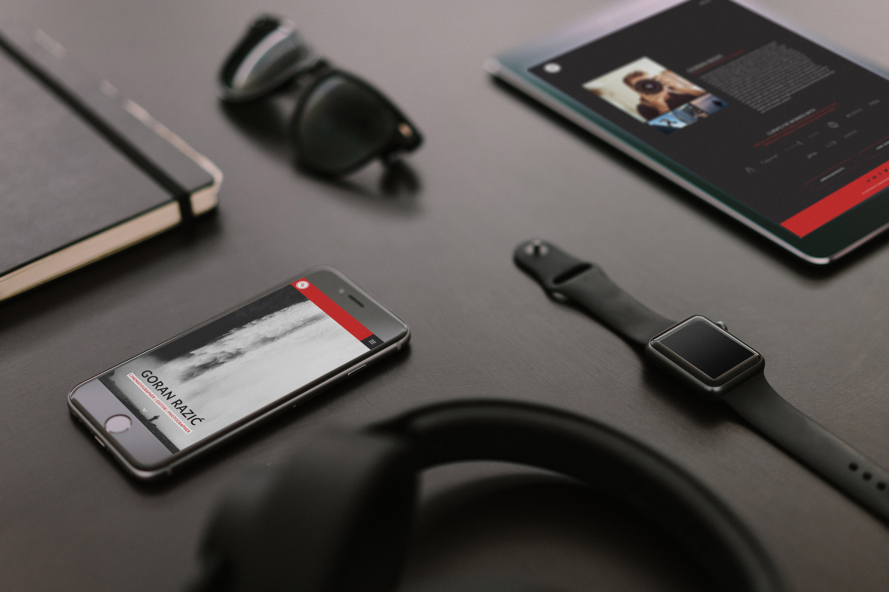 Smartphone and tablet showing Goran razic web pages on a table surrounded with gadgets